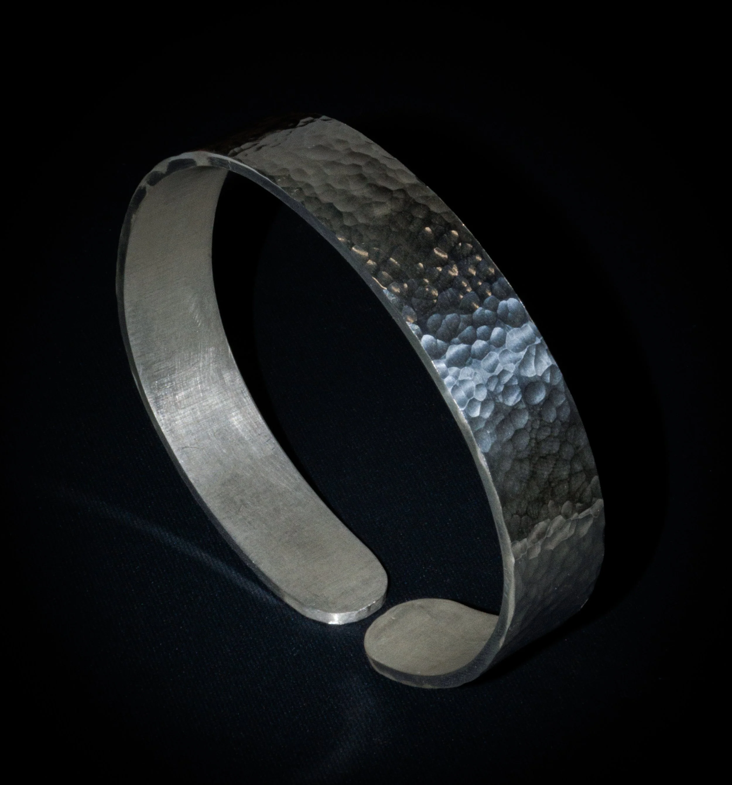Close-up of a metallic ring with textured and smooth surfaces on a dark background.
