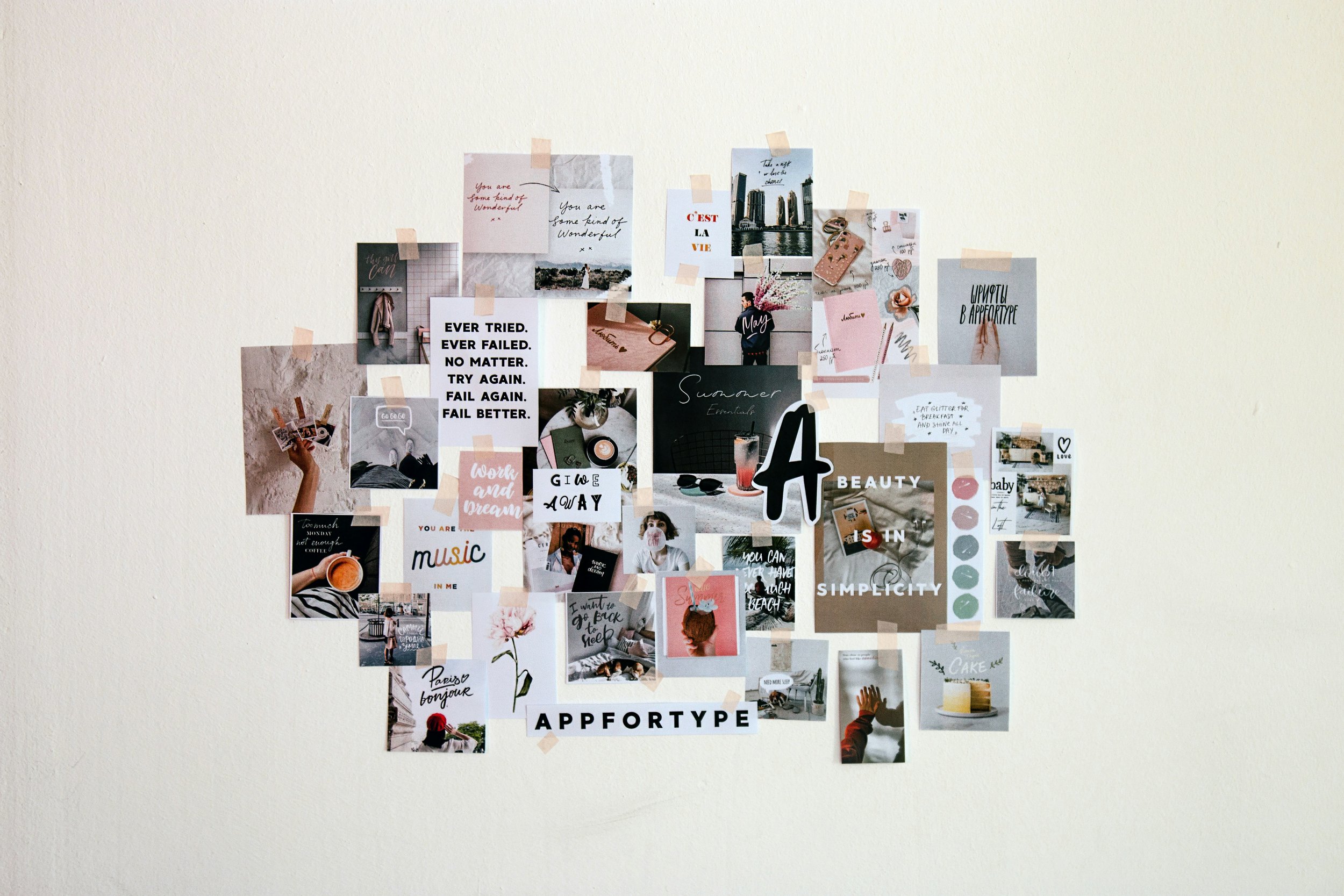 A wall decorated with a collage of various photos, notes, and artworks. The collage includes motivational quotes, cityscape images, floral photos, and personal pictures, all taped to the wall with light-colored tape.