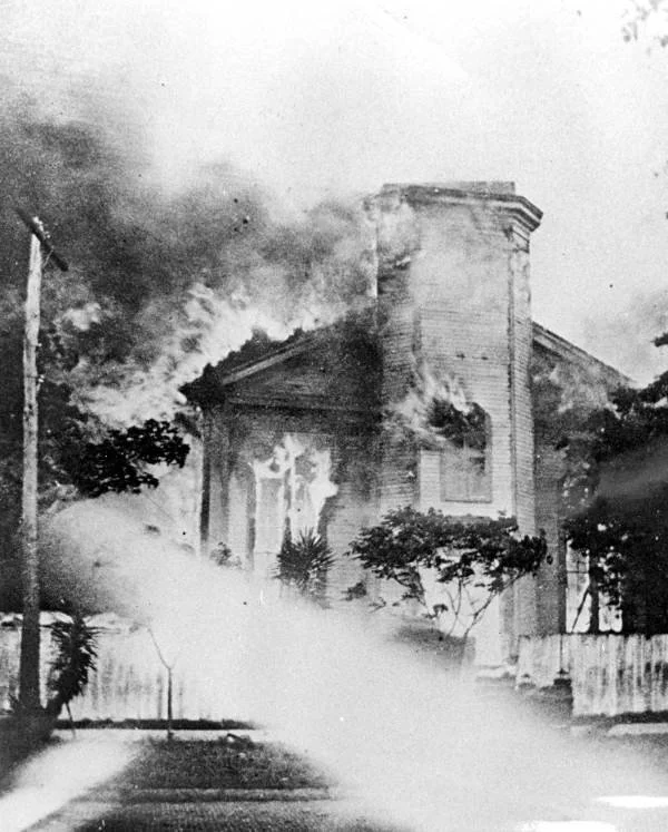 A church burning during the Great Fire of 1901 in Jacksonville, Florida, with heavy smoke and flames visible in the windows and roofline