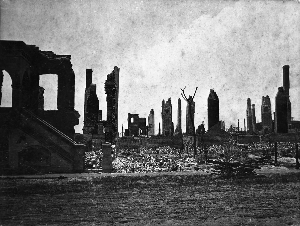 Black-and-white historical photograph of Jacksonville, Florida, after the Great Fire of 1901, showing a street lined with the ruins of burned buildings, crumbling brick walls, and debris.