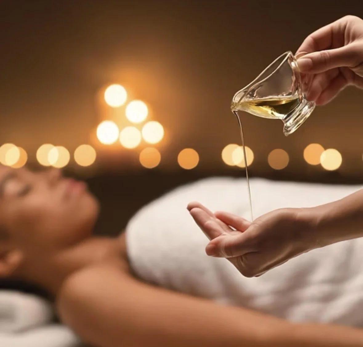 Person pouring oil or massage lubricant into palm of another person lying down with blurred background of warm glowing lights.