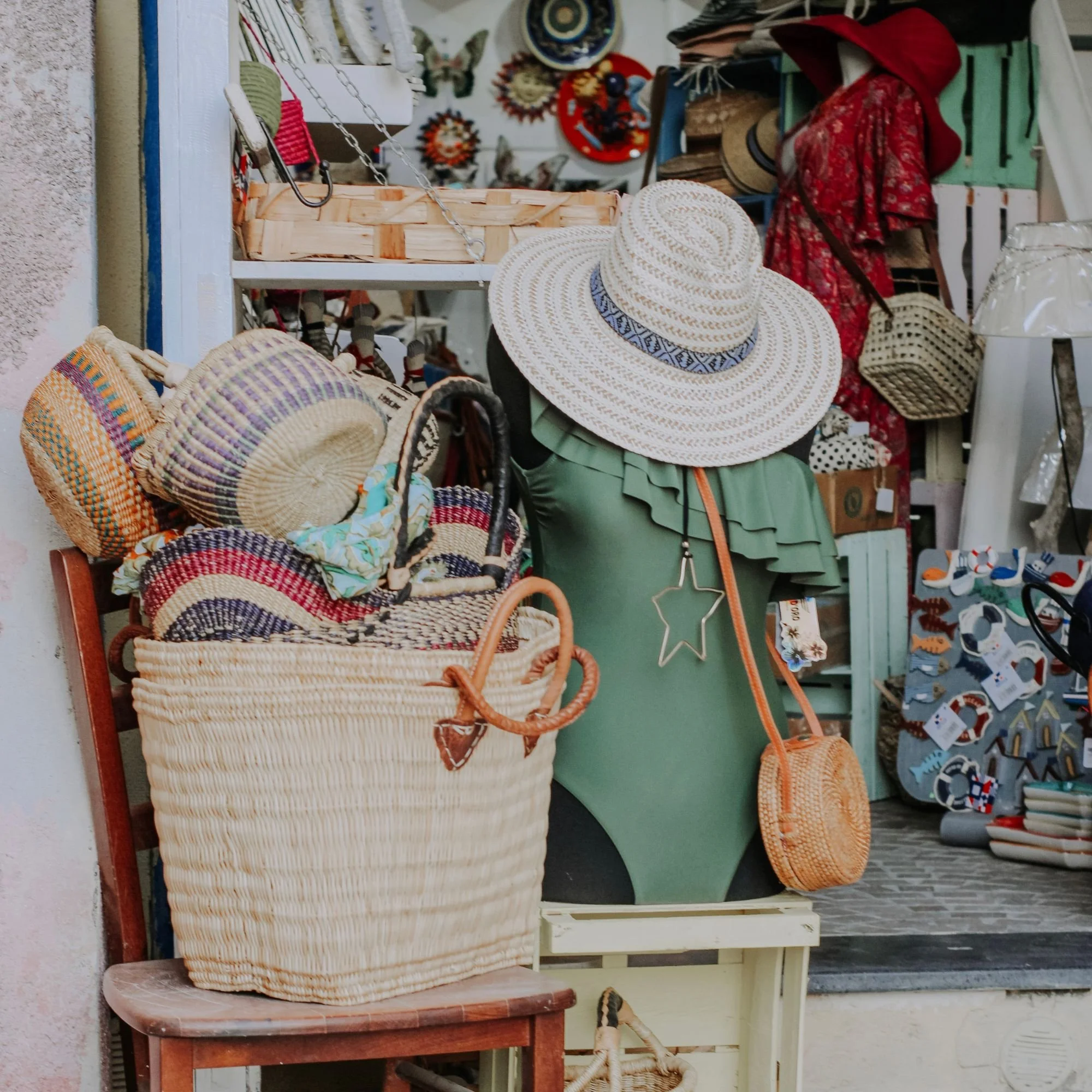 Display of woven straw hats, baskets, and accessories on shelves and a small table in a thrift store or boutique.
