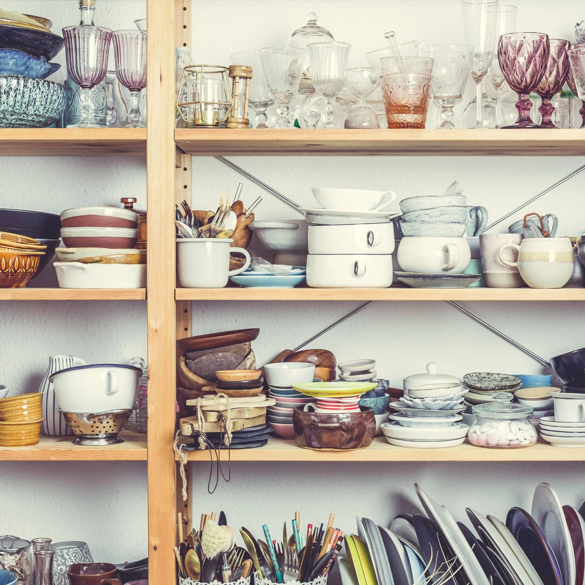 Kitchen shelves filled with glassware, bowls, mugs, plates, and utensils, organized on wooden shelves.