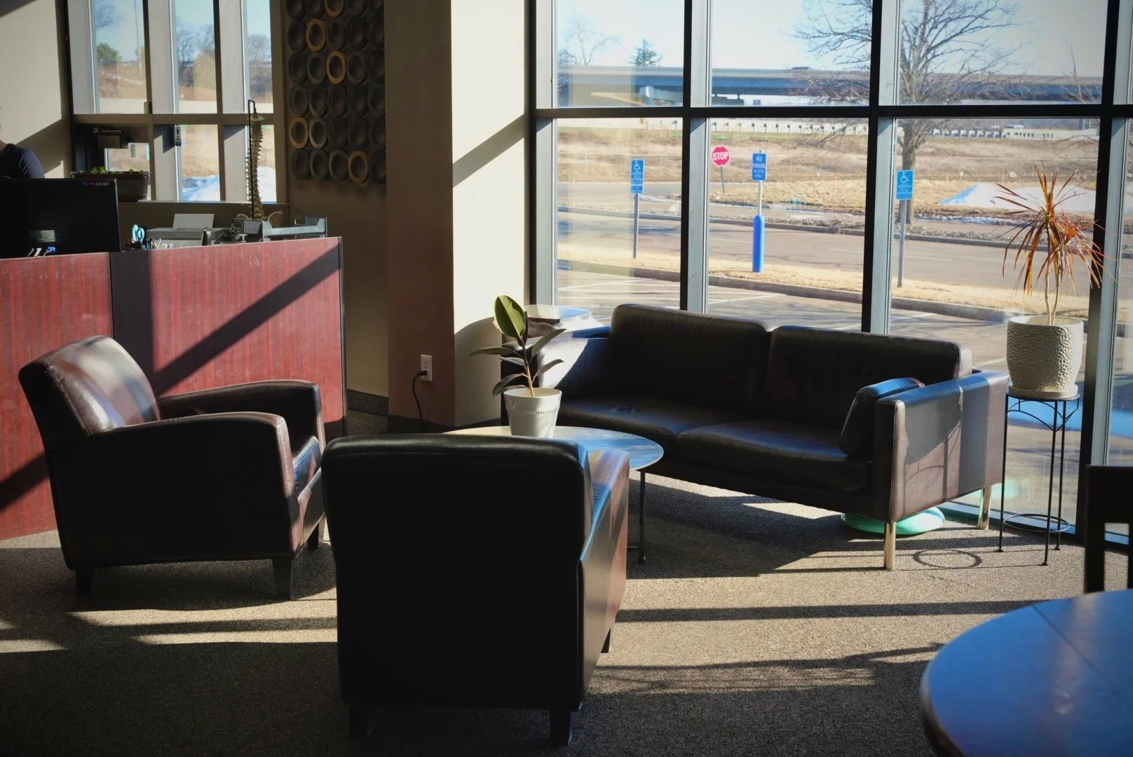 Interior of the ReVibe waiting area with black leather chairs and sofas, potted plants, and large windows showing a parking lot with snow and trees outside.