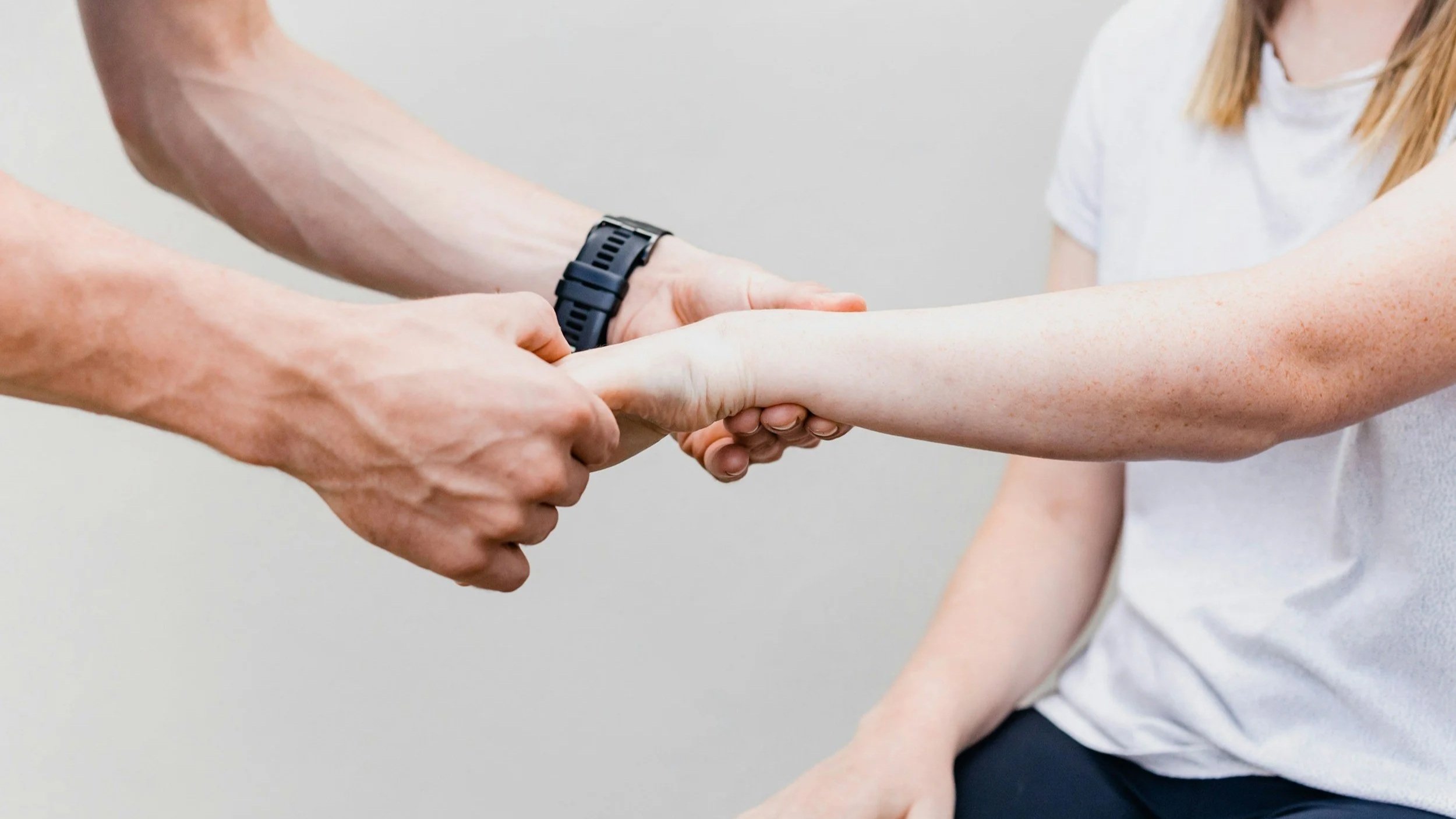 A clinician with a black watch on his wrist examines the arm and wrist of a woman.