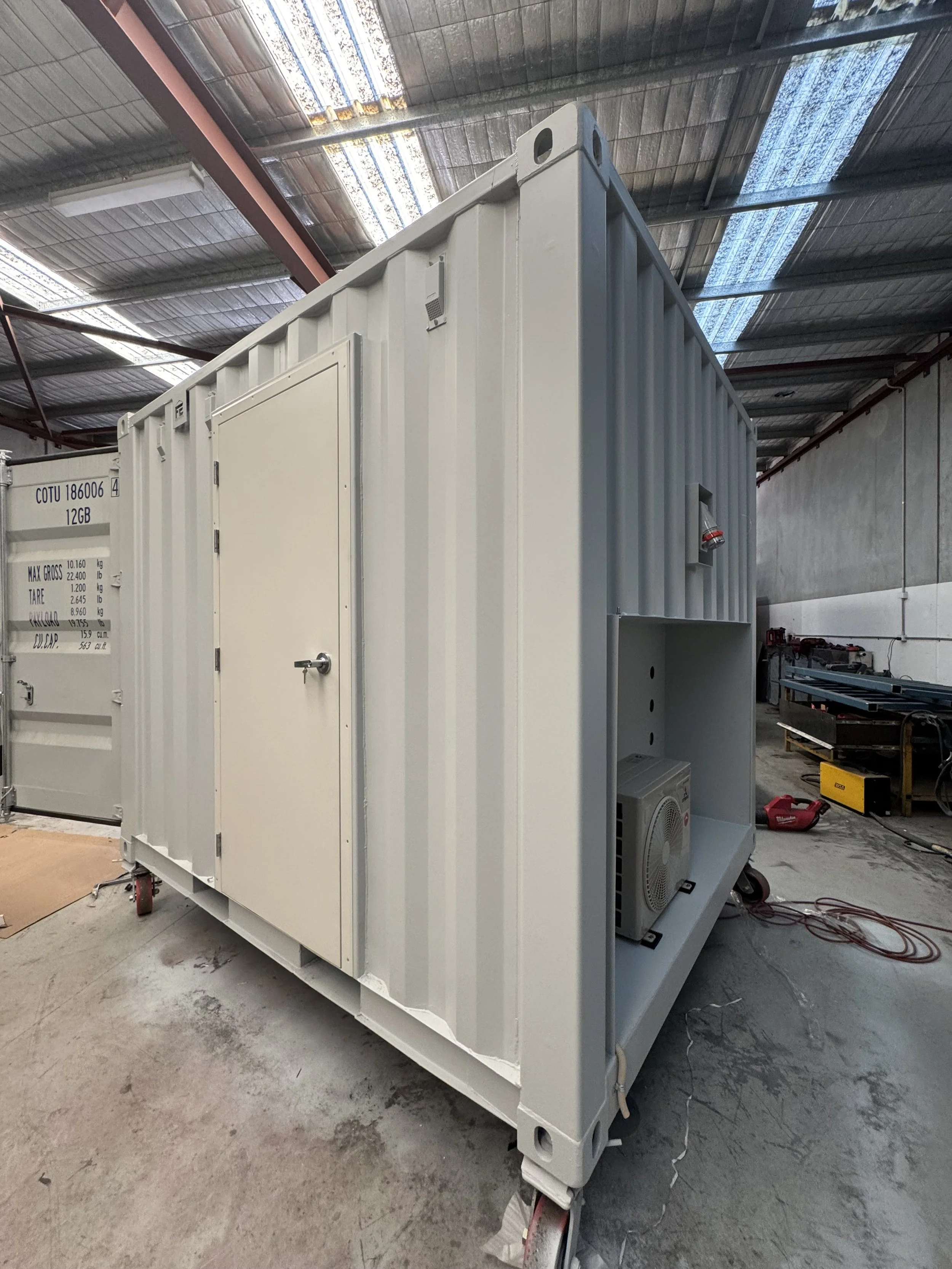 Industrial storage unit or electrical panel in a warehouse with tools and equipment around, some on wheels, in a large warehouse with a high ceiling and lighting.