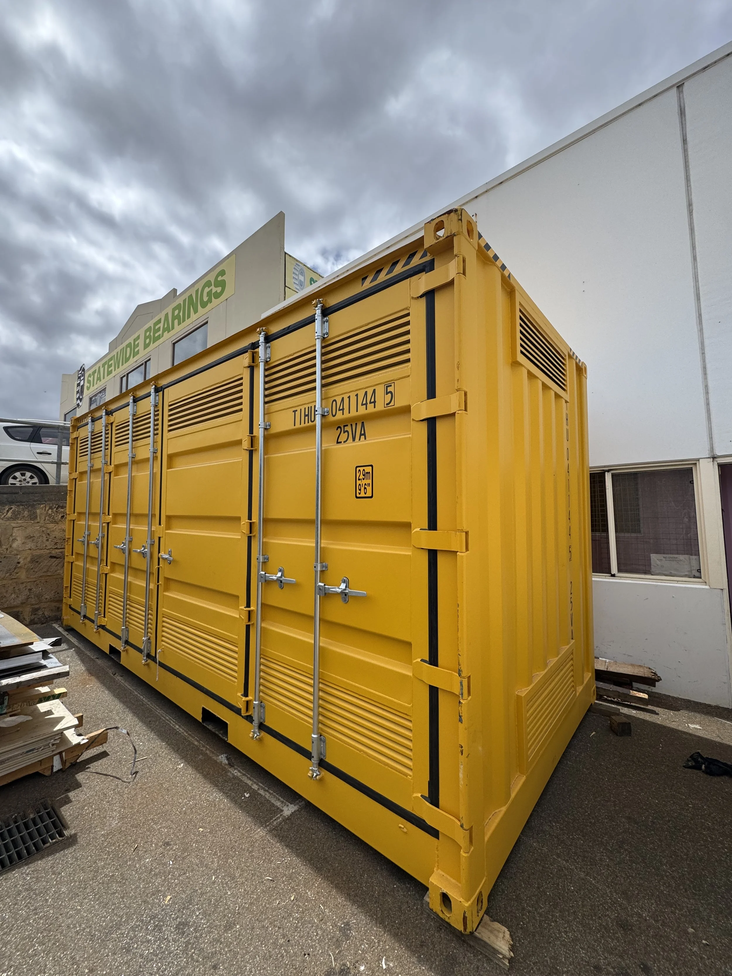 Large yellow industrial generator with black and yellow warning markings on a parking lot.