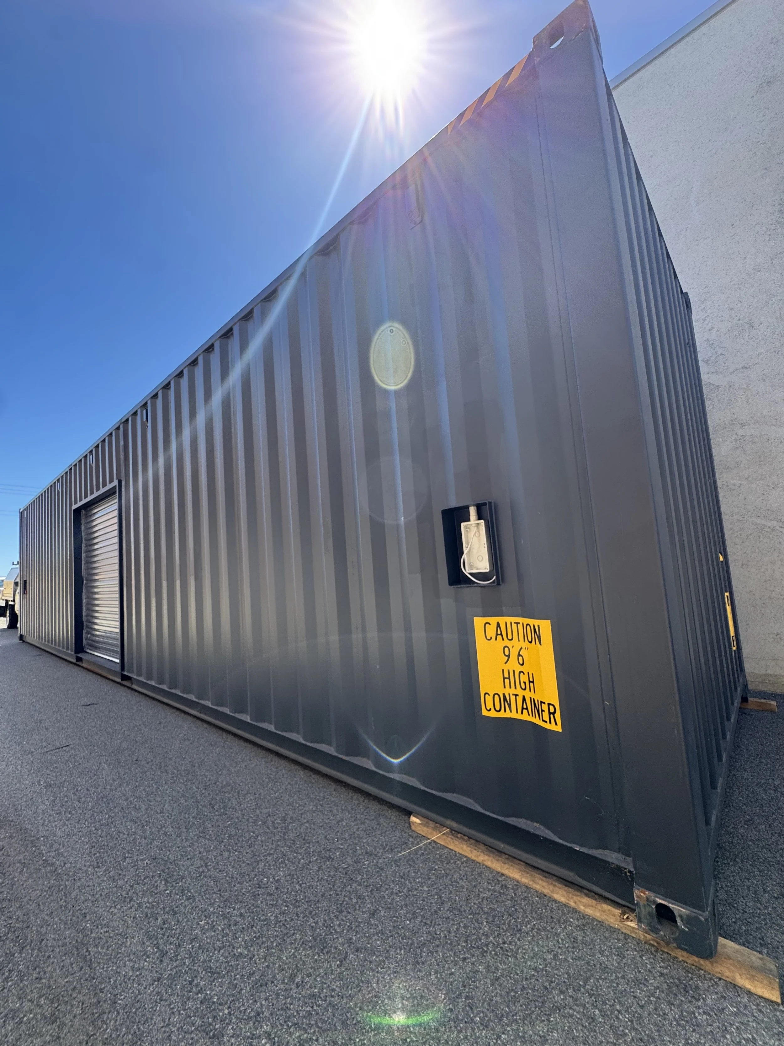 Large gray high container with a yellow caution sign that reads 'Caution 9'6" High Container' in an outdoor setting under a sunny blue sky.
