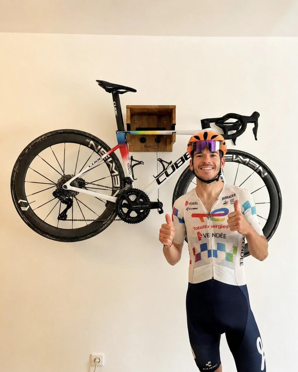 Cycliste professionnel (Nicolas Breuillard) devant son vélo de route installé sur un support vélo mural en bois