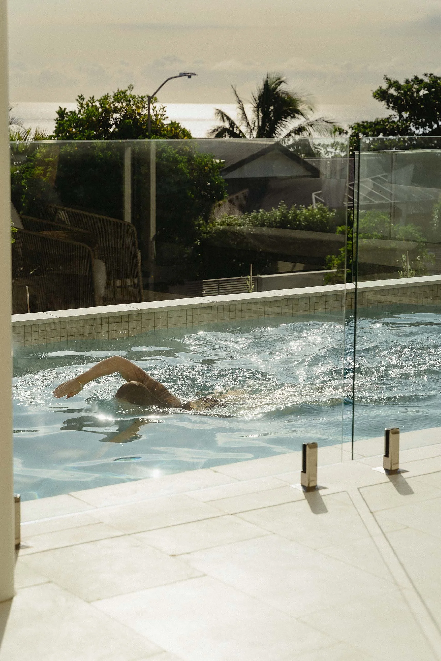 Person swimming behind frameless glass pool fencing with the ocean visible beyond at Horizon House, Sunrise Beach.