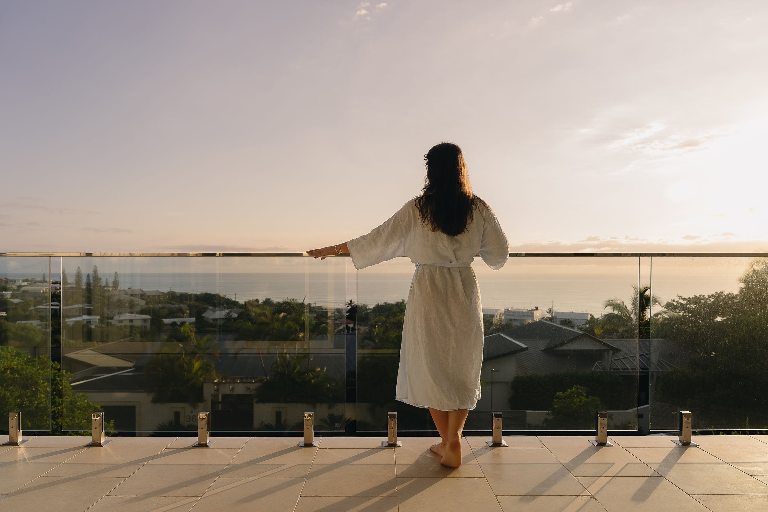 Woman standing behind a frameless glass balustrade overlooking the ocean at Horizon House in Sunrise Beach.