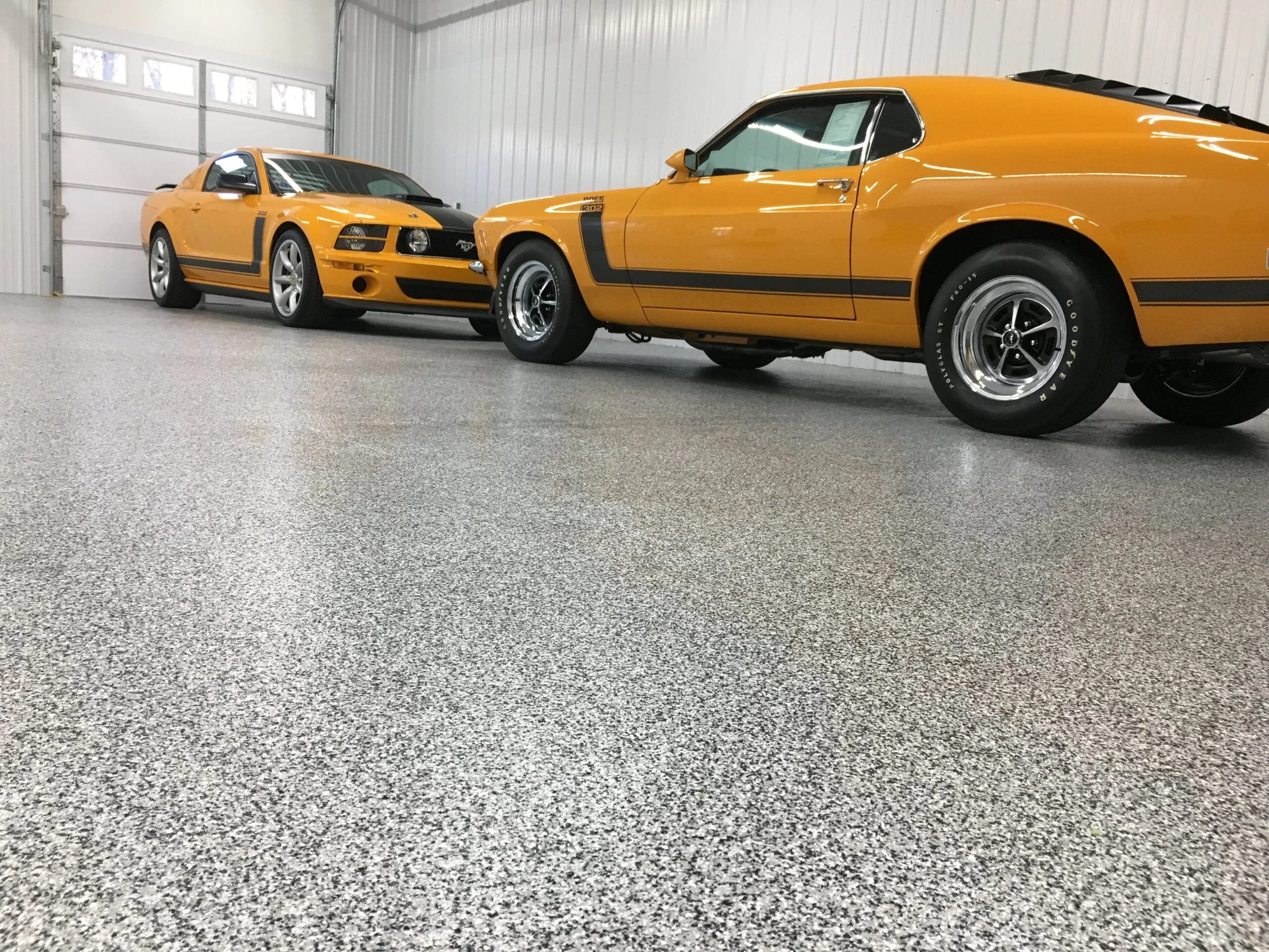 Two yellow Ford Mustangs parked in a garage with a grey speckled epoxy floor