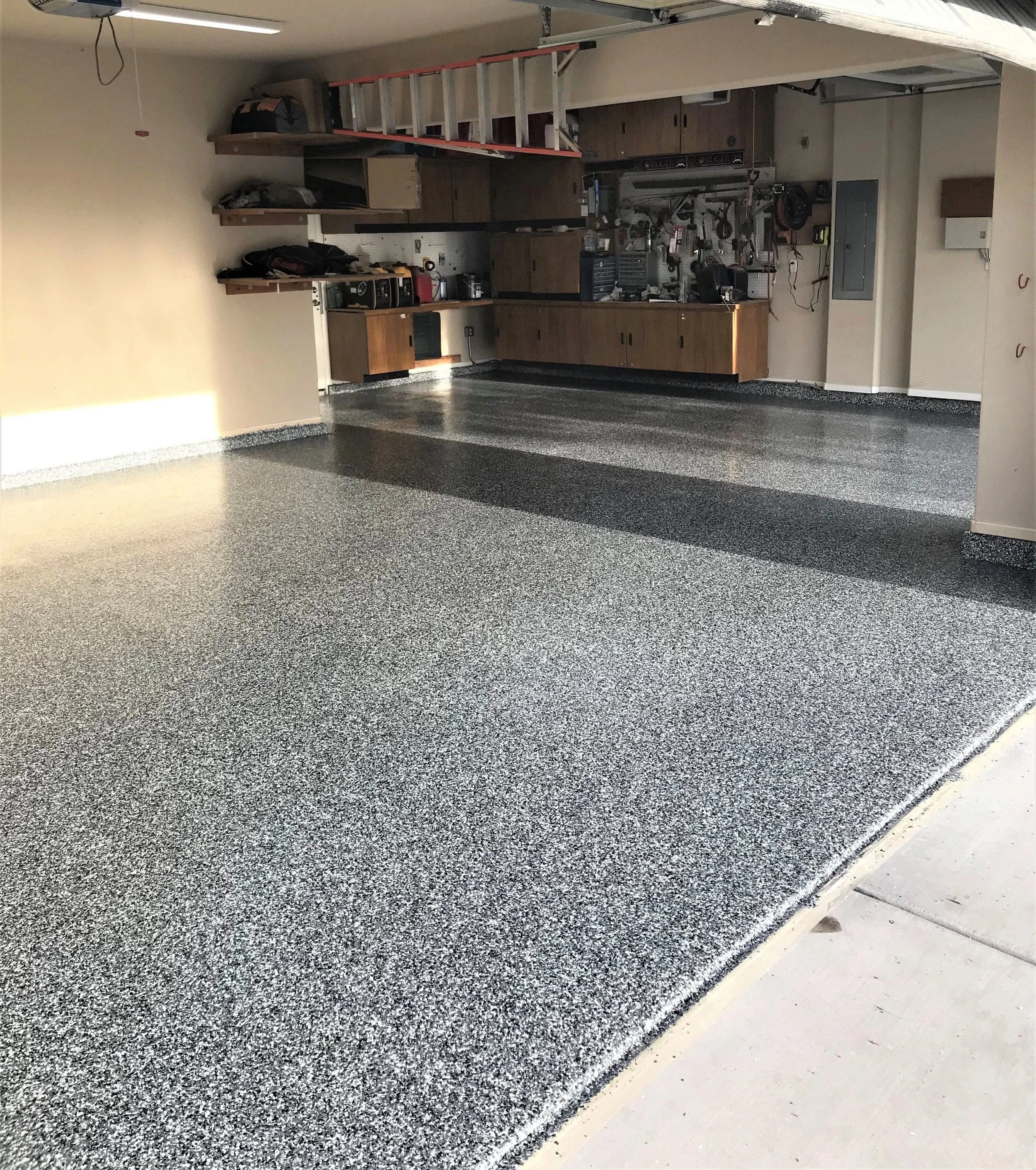 Large garage with wood cabinets along the back wall with a grey speckled epoxy floor