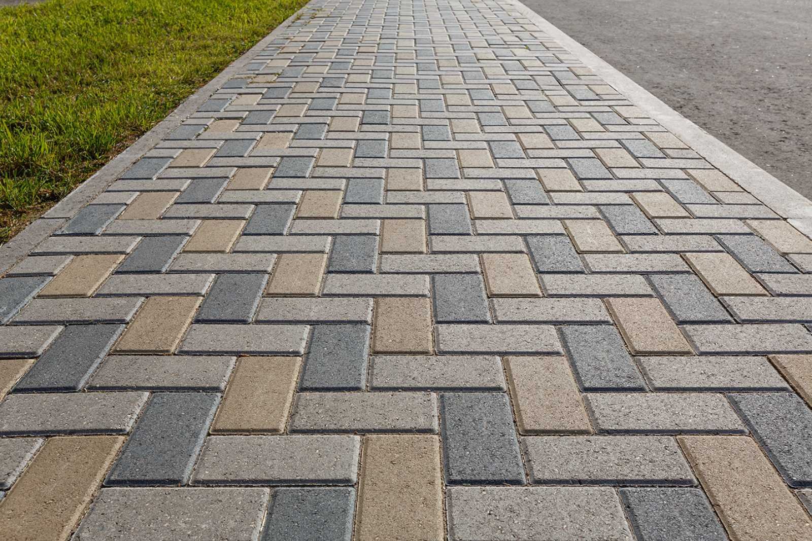 Light colored paver stones arranged in a herringbone style with grass on one side and pavement on the other side