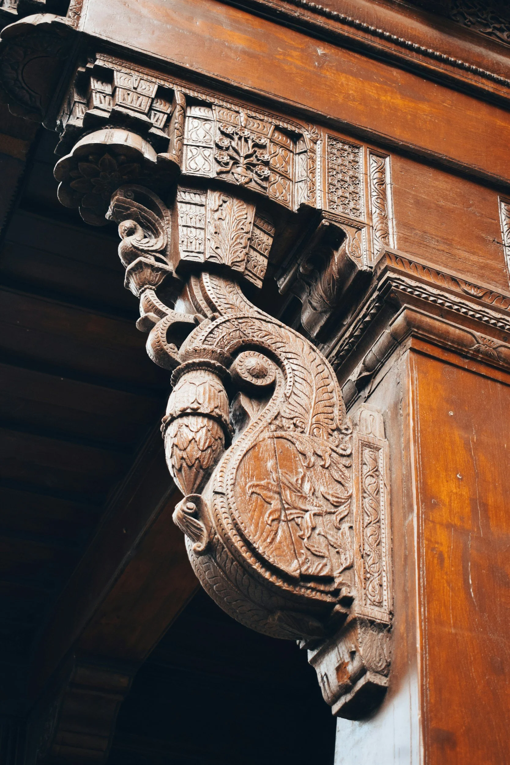Close-up of an intricately carved wooden corbel supporting a wooden beam with detailed geometric and floral patterns.