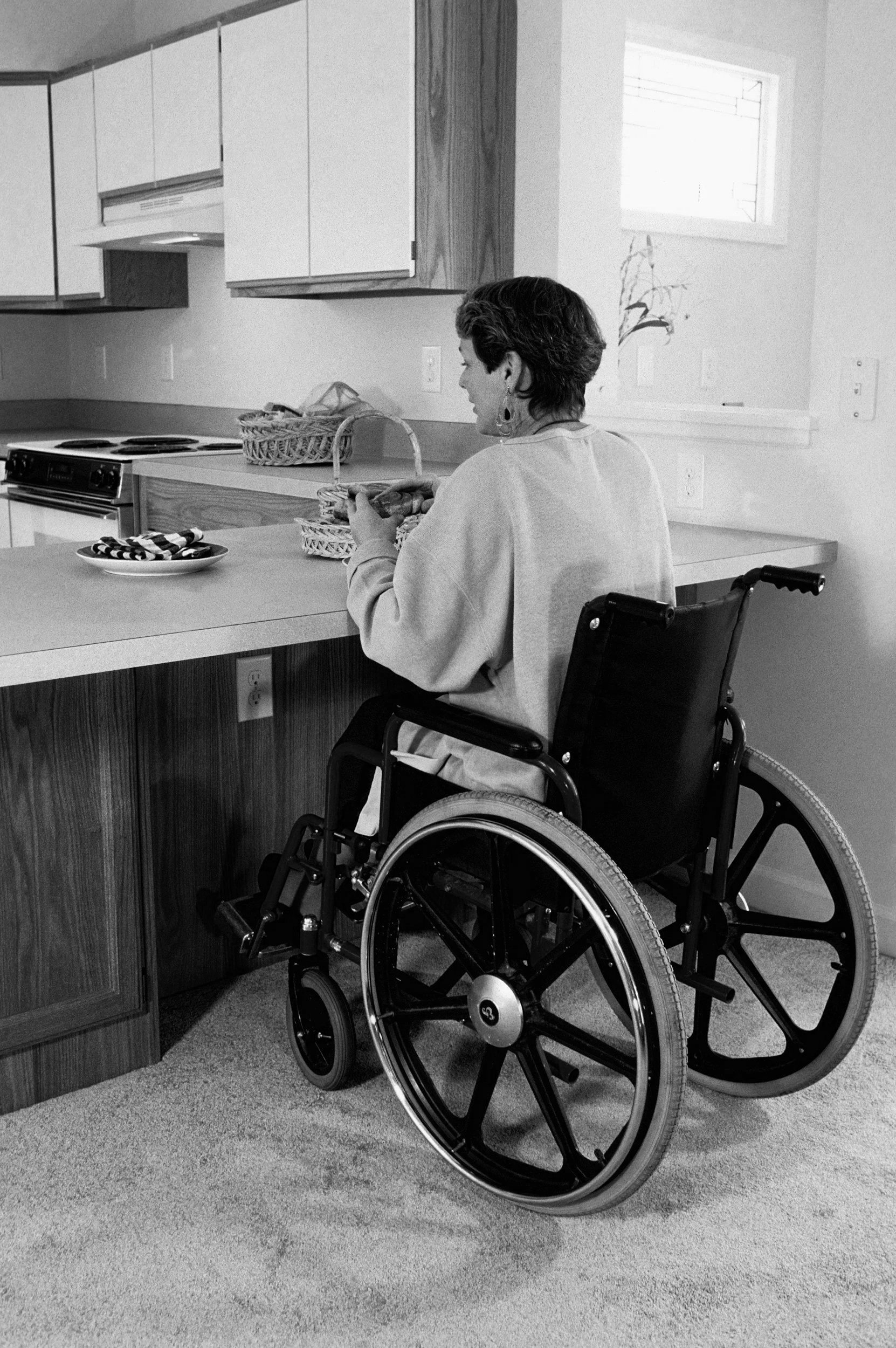 A woman in a wheelchair in a kitchen preparing food on a countertop.