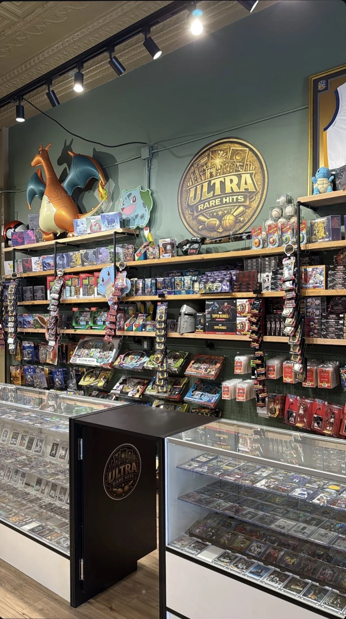 A display of trading cards and collectibles in a store, with Pokémon-themed balloons and a sign reading 'ULTRA RARE HITS'.