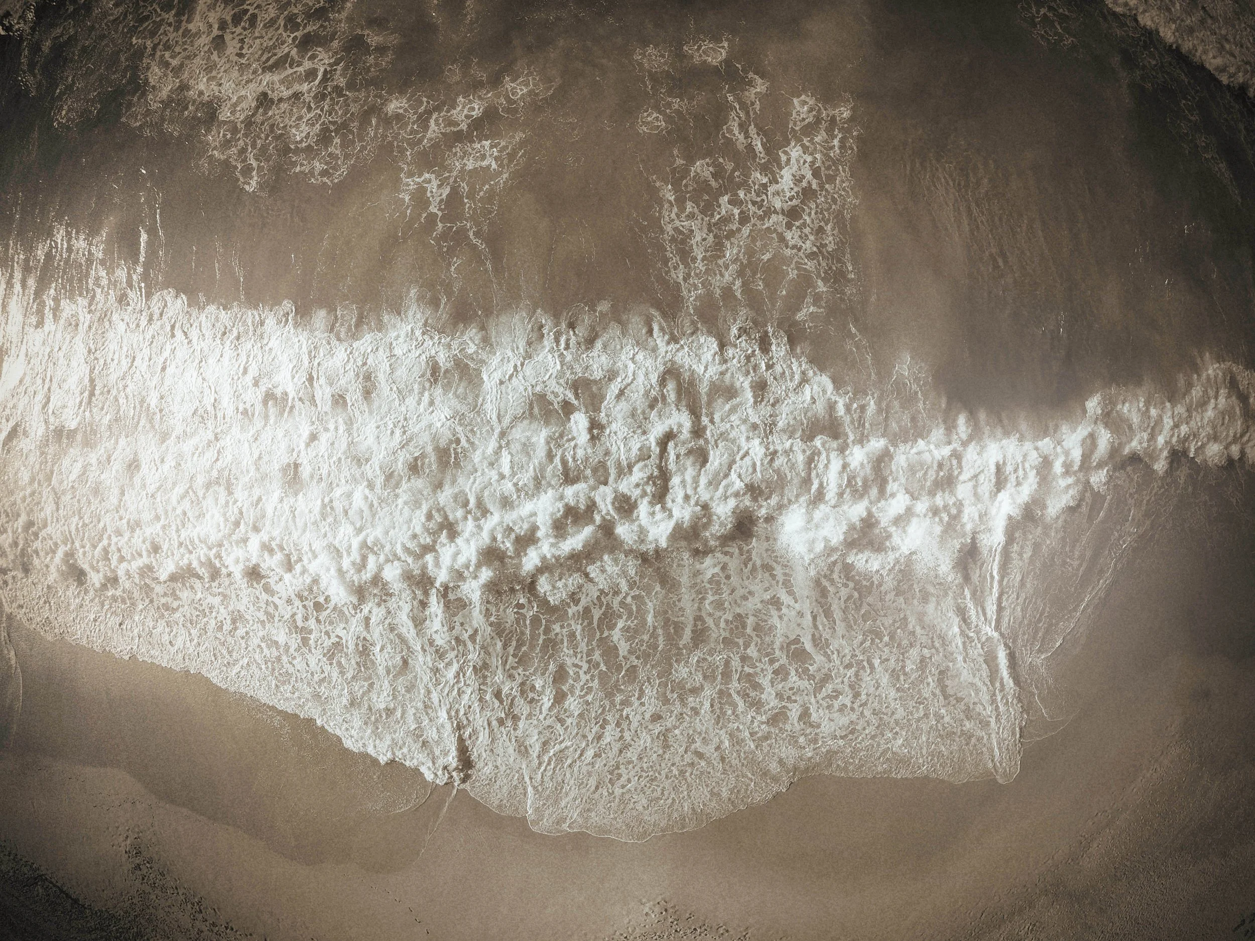 Aerial view of ocean waves crashing onto sandy beach