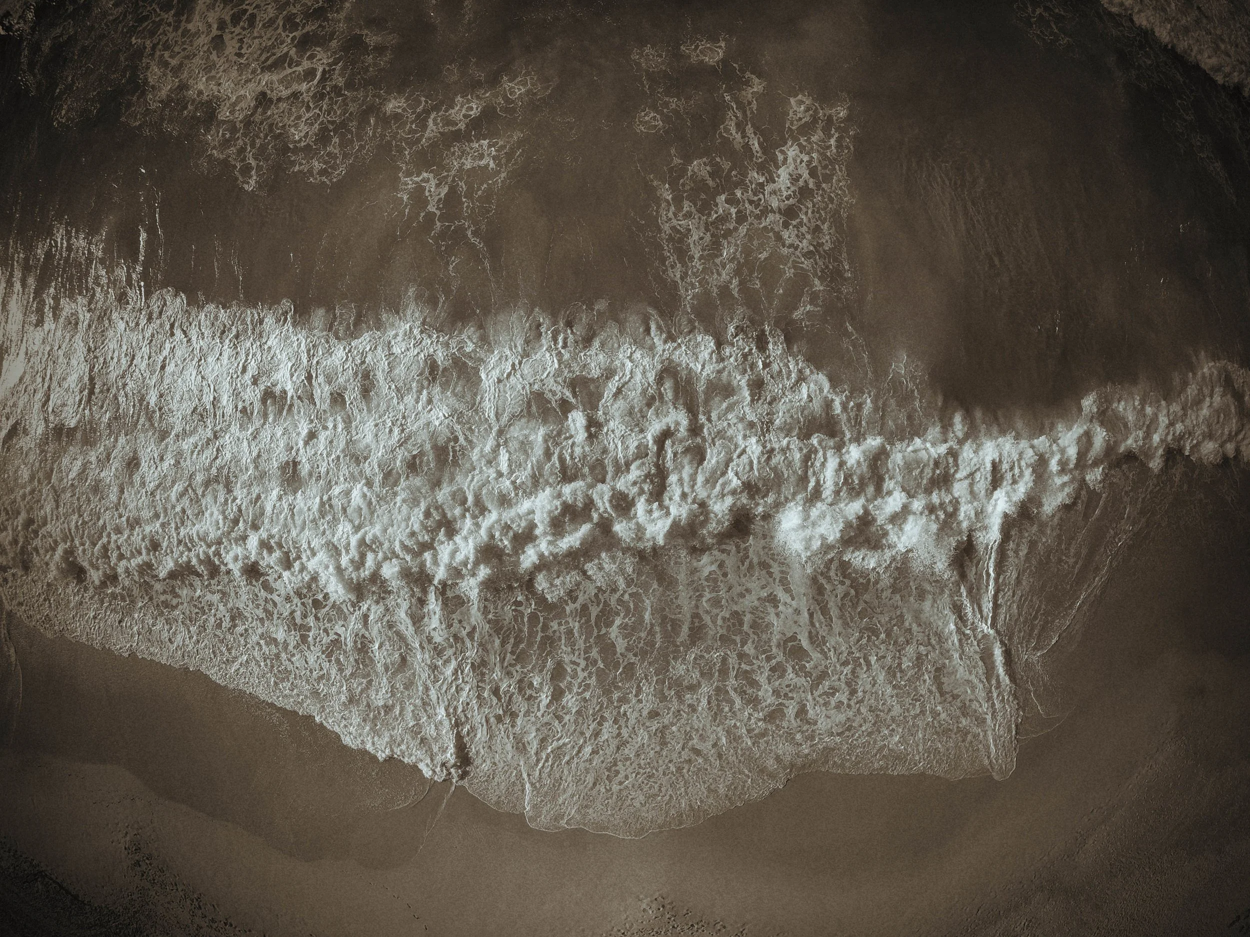 An aerial view of ocean waves crashing onto the sandy shore.