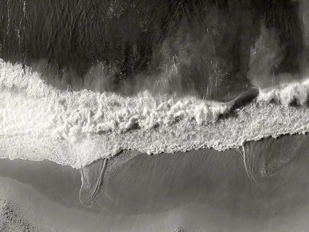 Close-up of ocean waves crashing and foaming on the shore from an aerial perspective.