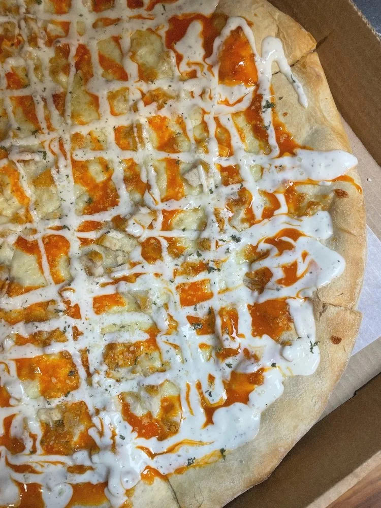 Pizza with orange and white sauce drizzle, containing cheese and possibly chicken or seafood, in a cardboard box.