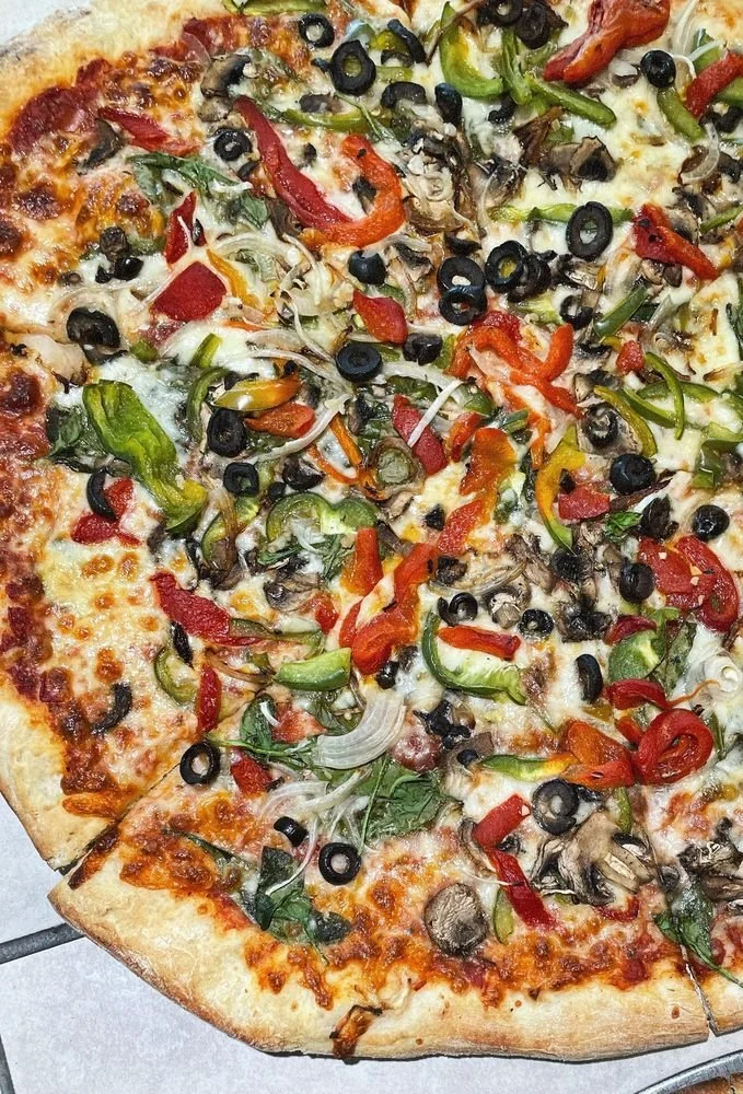 A slice of vegetable pizza with cheese, black olives, green peppers, red peppers, onions, and mushrooms on a thin crust.
