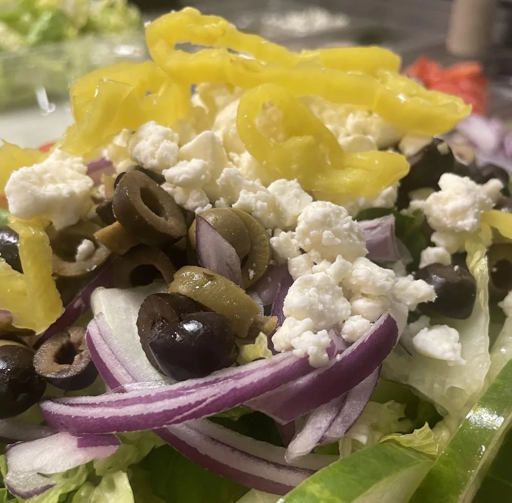 Close-up of a fresh salad with black olives, chopped red onions, shredded lettuce, and crumbled feta cheese.