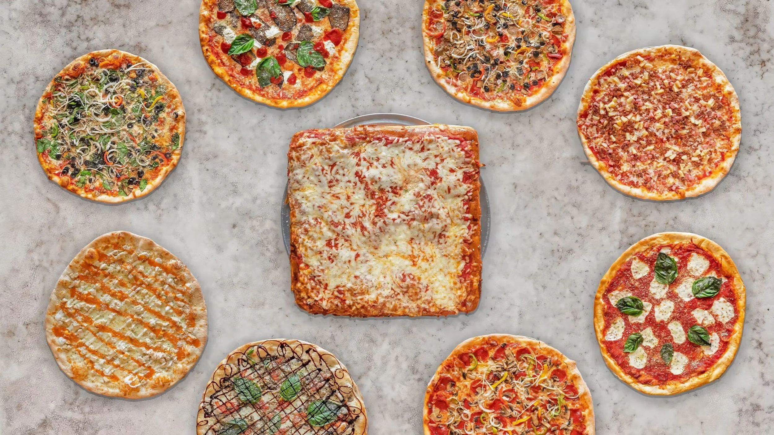 A variety of different pizzas with various toppings arranged on a gray surface