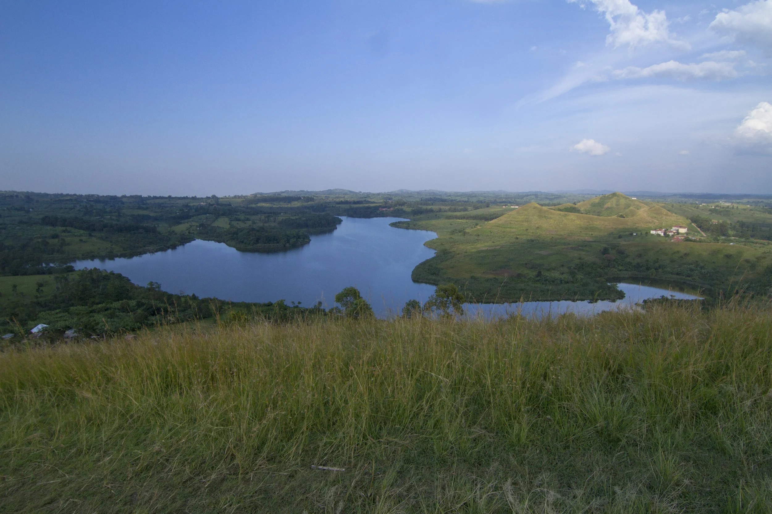 A scenic landscape showing a river winding through green hills and fields under a blue sky with scattered clouds.