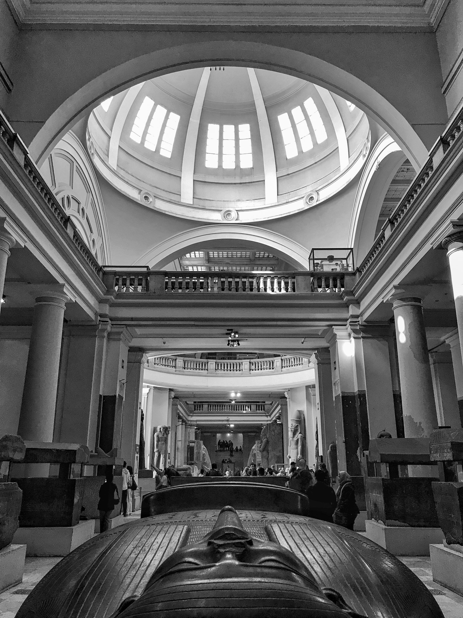 A black-and-white photo of a grand, historic interior with a high domed ceiling and large windows allowing natural light to fill the space. The view is from the front of a vehicle, looking up towards the ceiling, showing ornate architectural details 