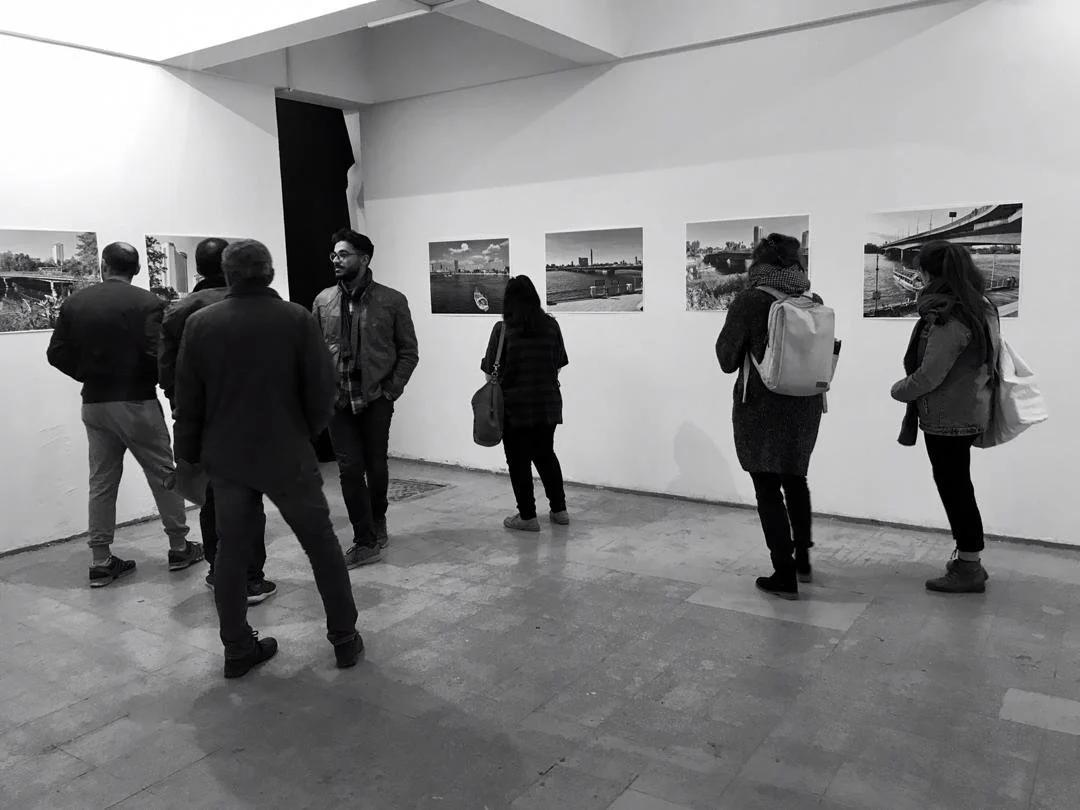 People viewing the photographs of the Bridging the Nile exhibition displayed on a white gallery wall at Darb in Cairo, Egypt.