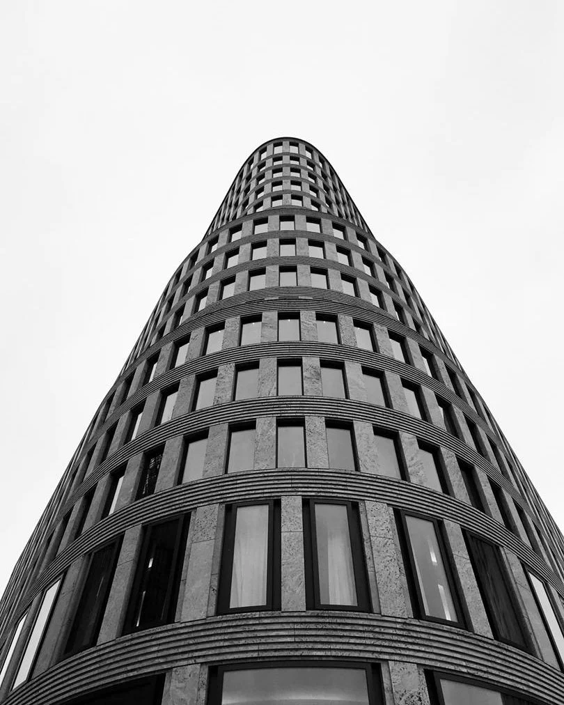 A tall, modern, cylindrical building with many windows, seen from ground level looking up.