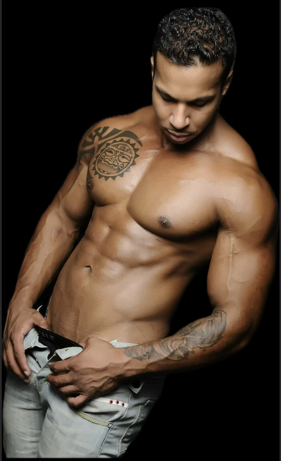 A shirtless man with tattoos on his chest, arm, and shoulder flexing his muscles against a black background. male stripper, bachelorette,  girls's night