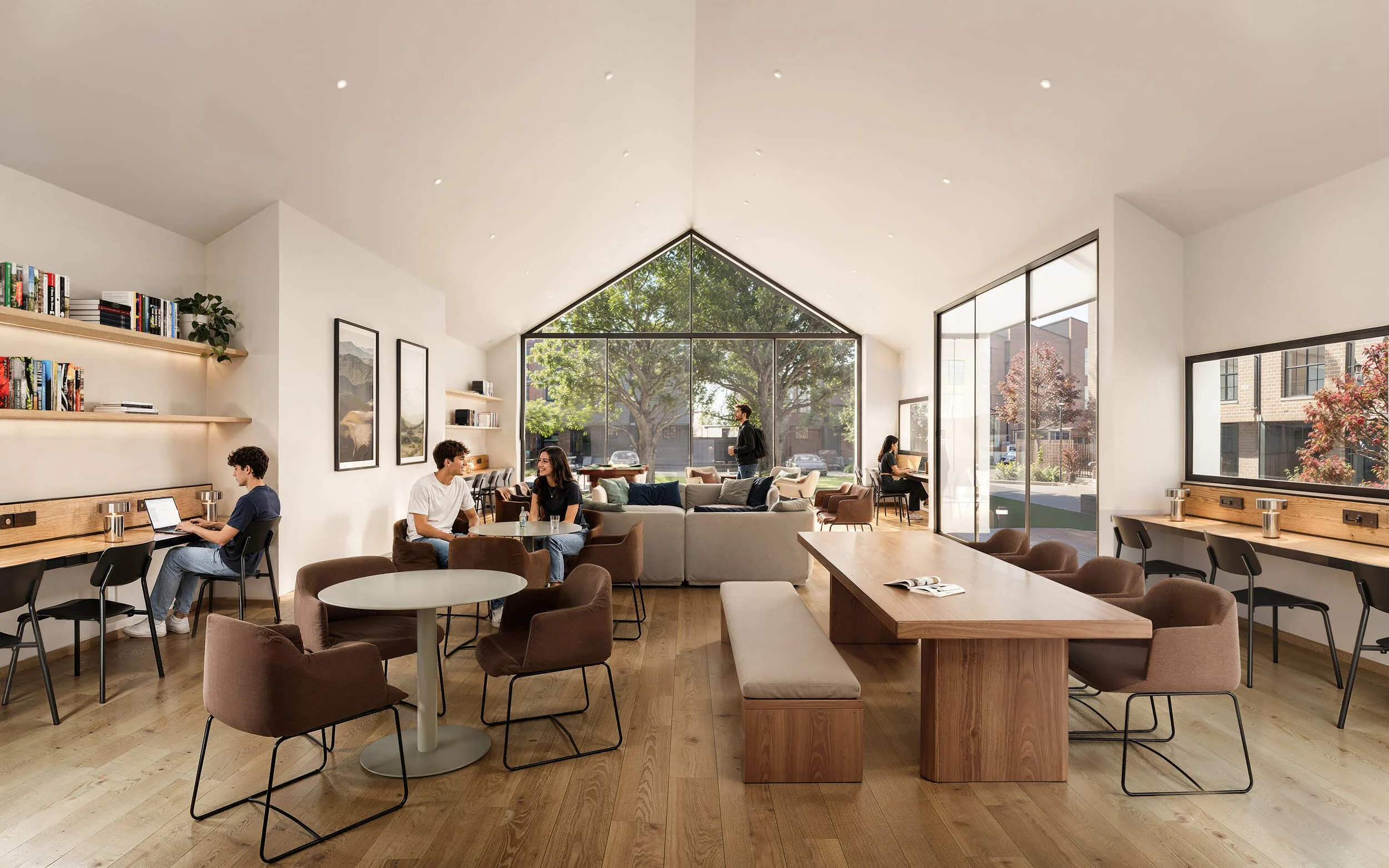 Bright, modern coffee shop with large glass front and tall ceiling. Several people are sitting and working or talking, with bookshelves and artwork on the walls.