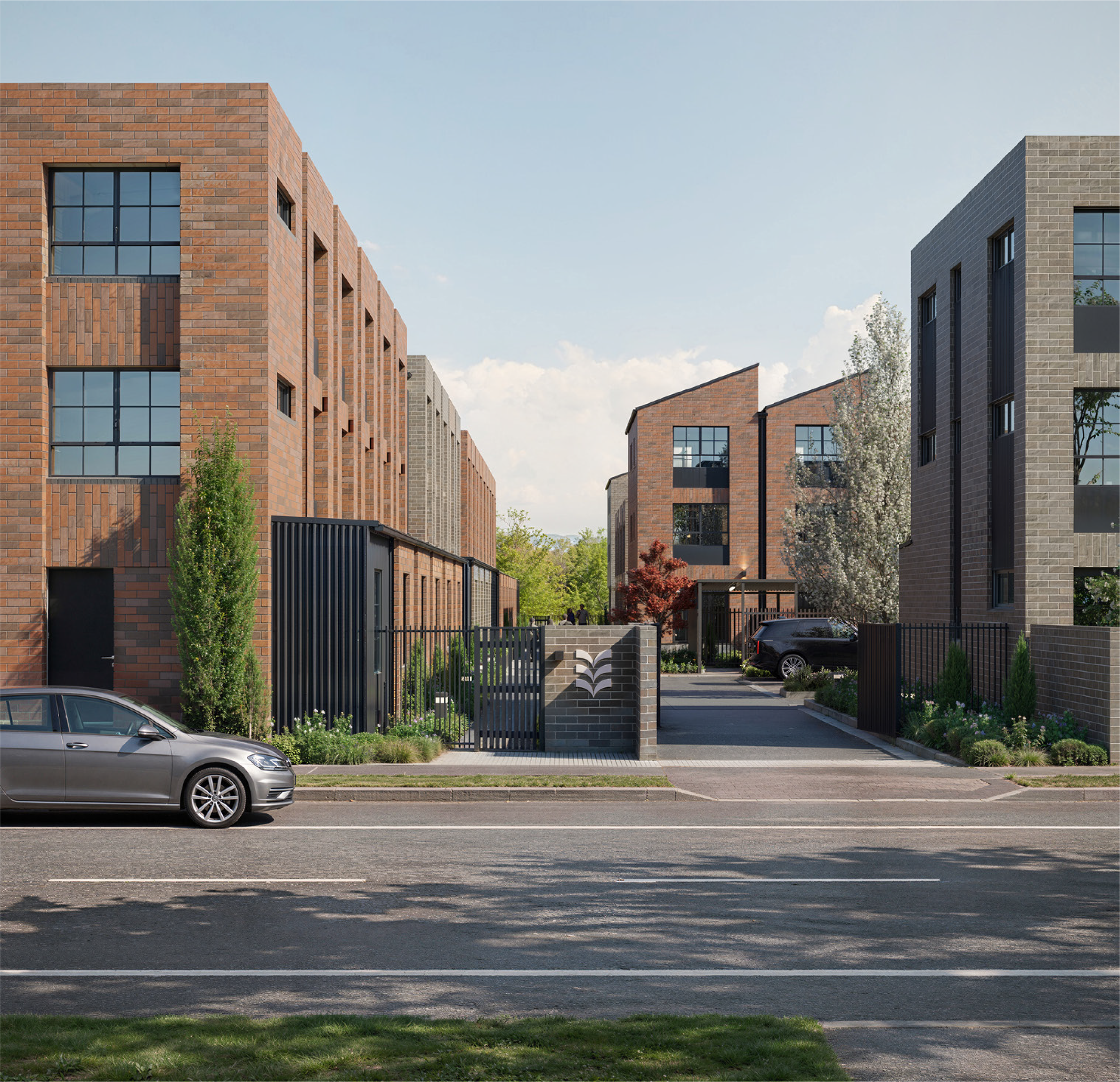 Modern multi-story residential buildings with brick and gray brick facades, black-framed windows, a black metal fence, and a parking lot with a silver car, green trees, and a blue sky with some clouds in the background.