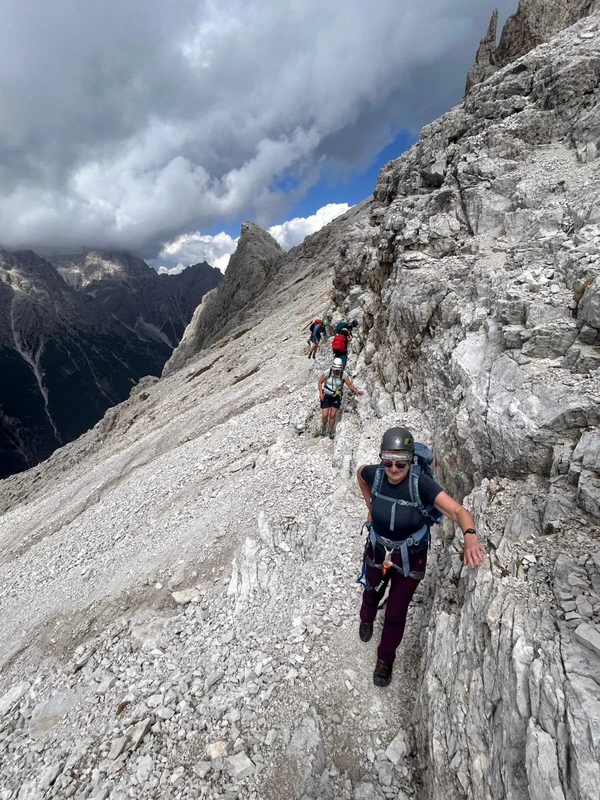 Group of climbers ascending a steep rocky mountain trail with dramatic clouds overhead.