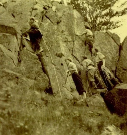 A group of seven men rock climbing on a steep outdoor rock face, using ropes and gear for safety.
