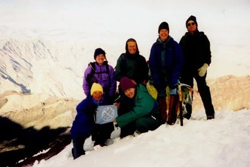 Group of five people in winter clothing hiking in a snowy landscape with mountains in the background.