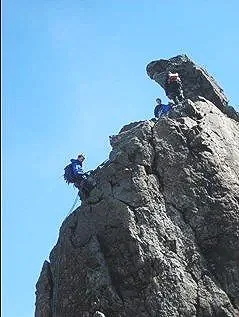 A person climbing a rocky mountain with a dog at the top on a sunny day.
