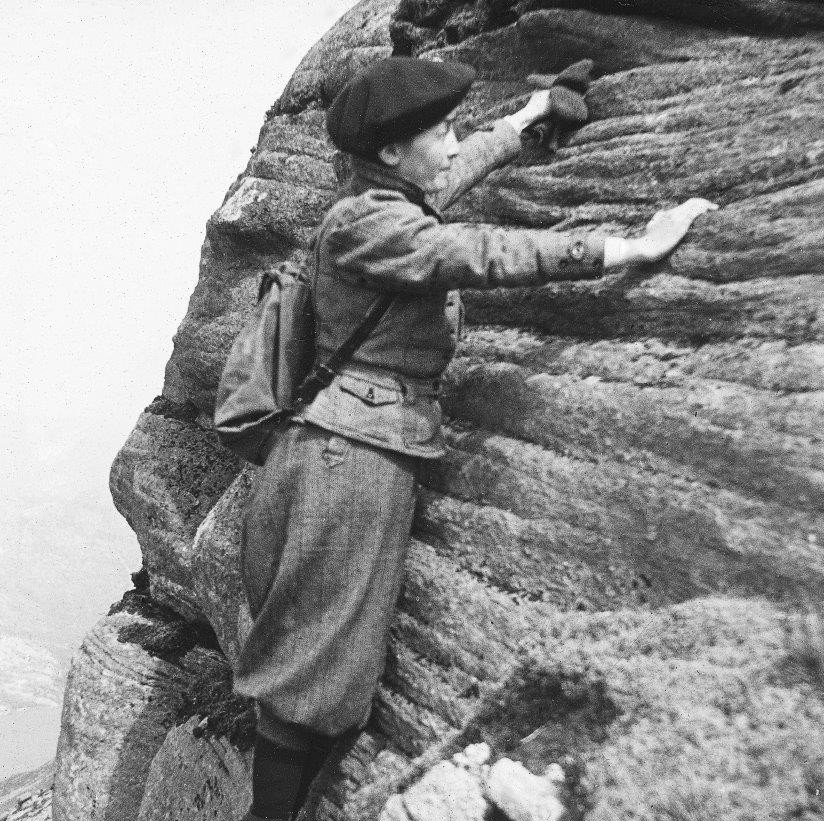 A person wearing a coat, hat, and backpack climbing a rocky cliff.