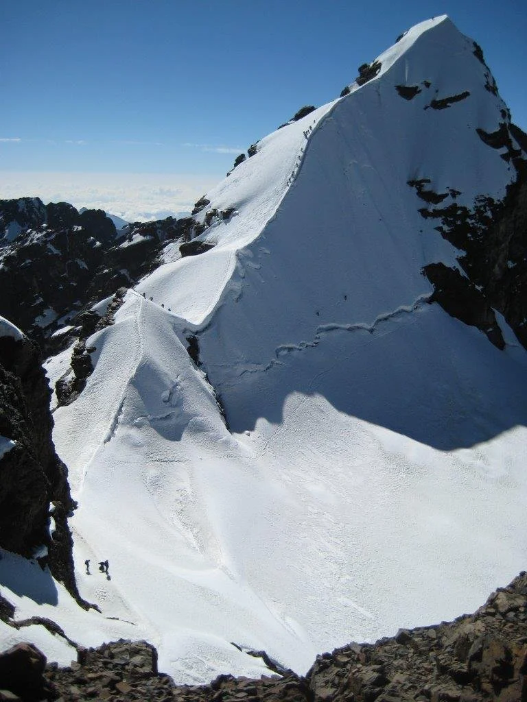 Snow-covered mountain peak with two climbers ascending the icy slopes.