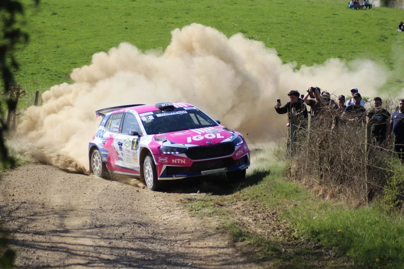 Une voiture de rallye colorée passant près d'une foule de spectateurs à l'extérieur, provoquant un nuage de poussière.