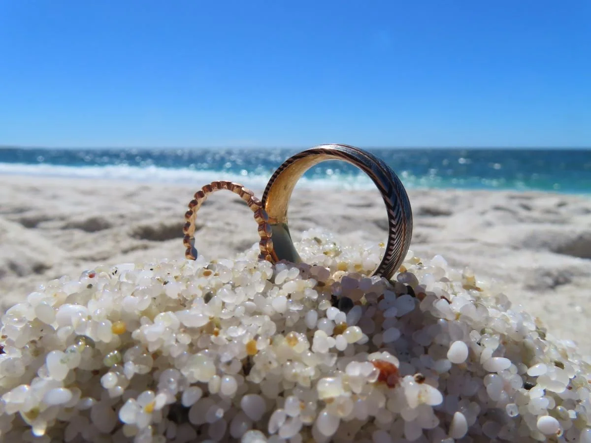 Deux anneaux en bois plantés dans du sable blanc avec la mer et un ciel bleu en arrière-plan.