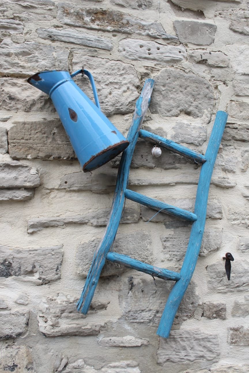 Une vieille lampe bleue fixée à un mur en pierre, avec un support en bois peint en bleu également, donnant l'impression d'une chaise