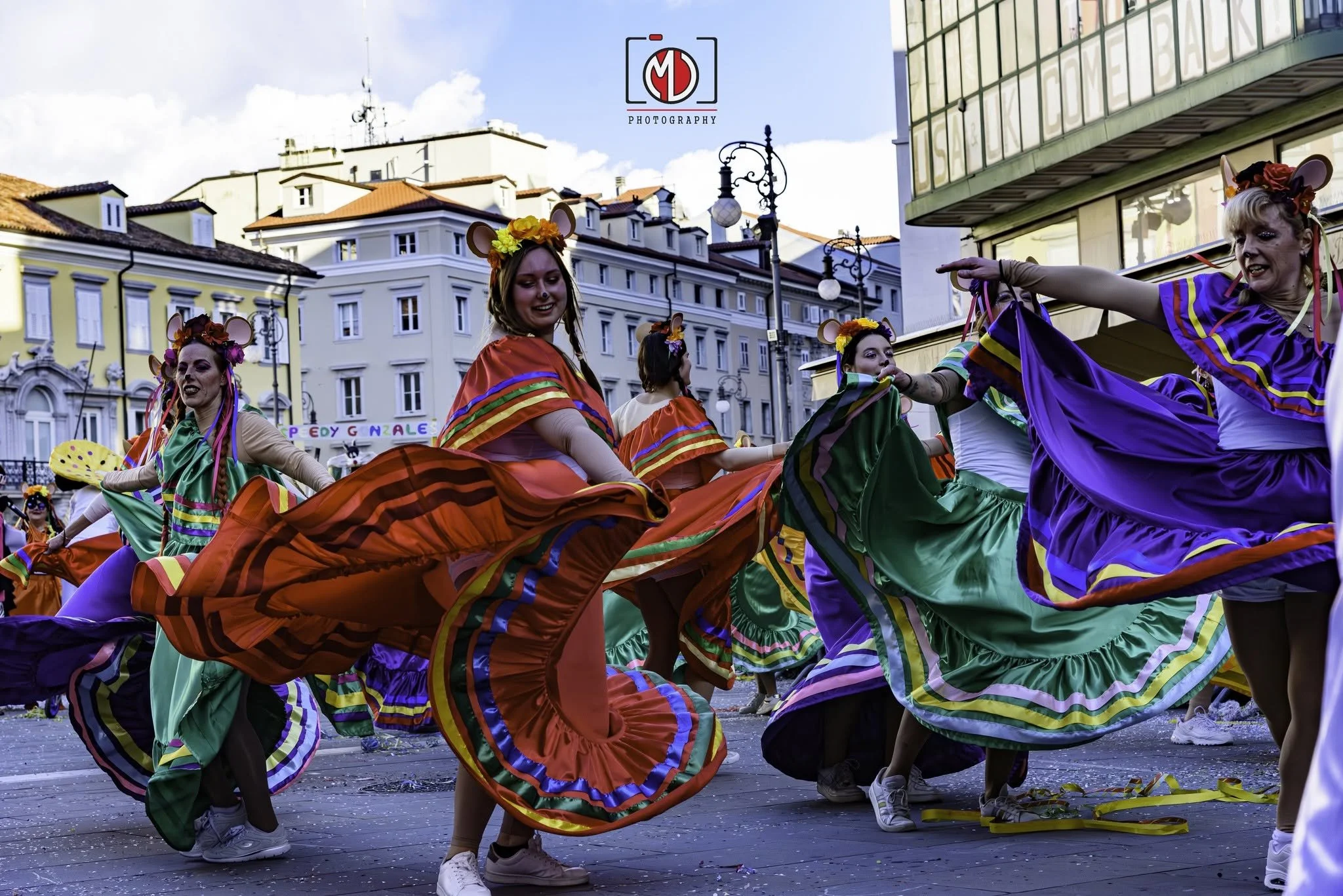 Gruppo di persone che ballano in maschera colorata durante una festa all'aperto in una piazza urbana