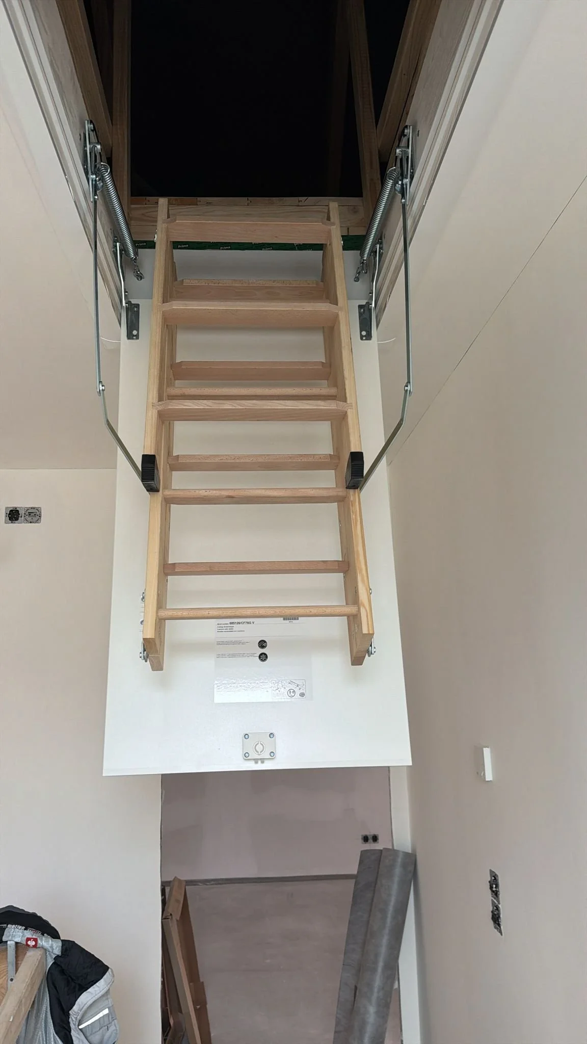 Holztreppe in einem Raum, die in ein Dachgeschoss führt, mit Geländern aus Metall und Schaumstoffkappen an den Enden.