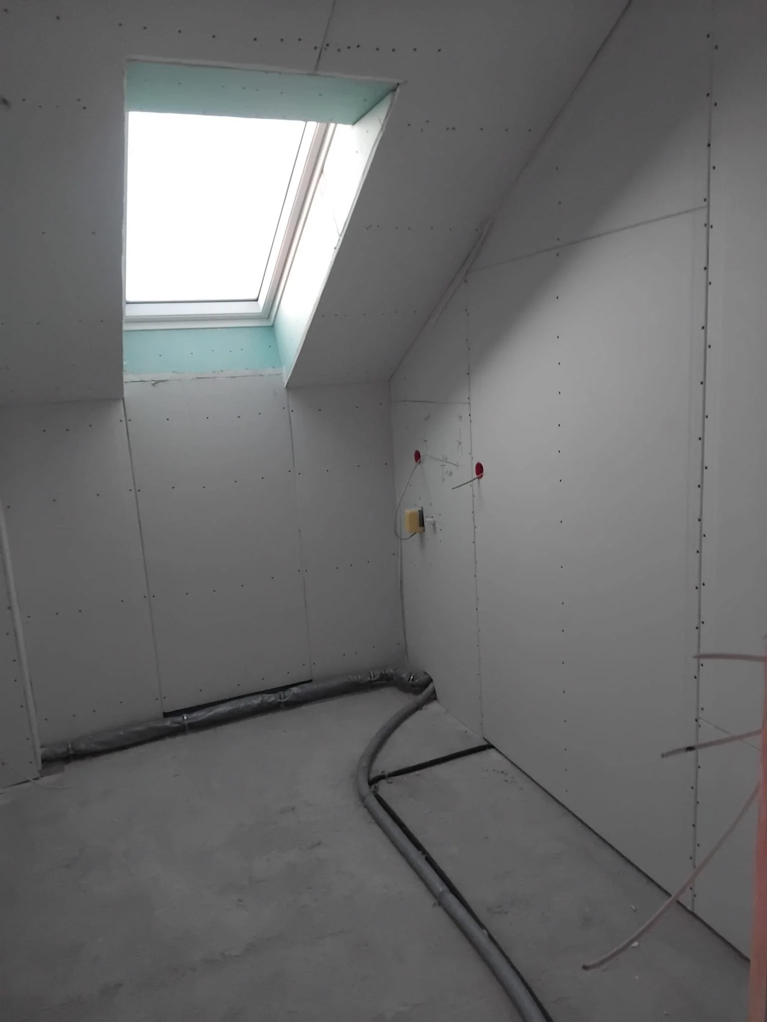 Innenraum eines unvollendeten Zimmers mit installierter Dachgaube und sichtbaren elektrischen Leitungen.