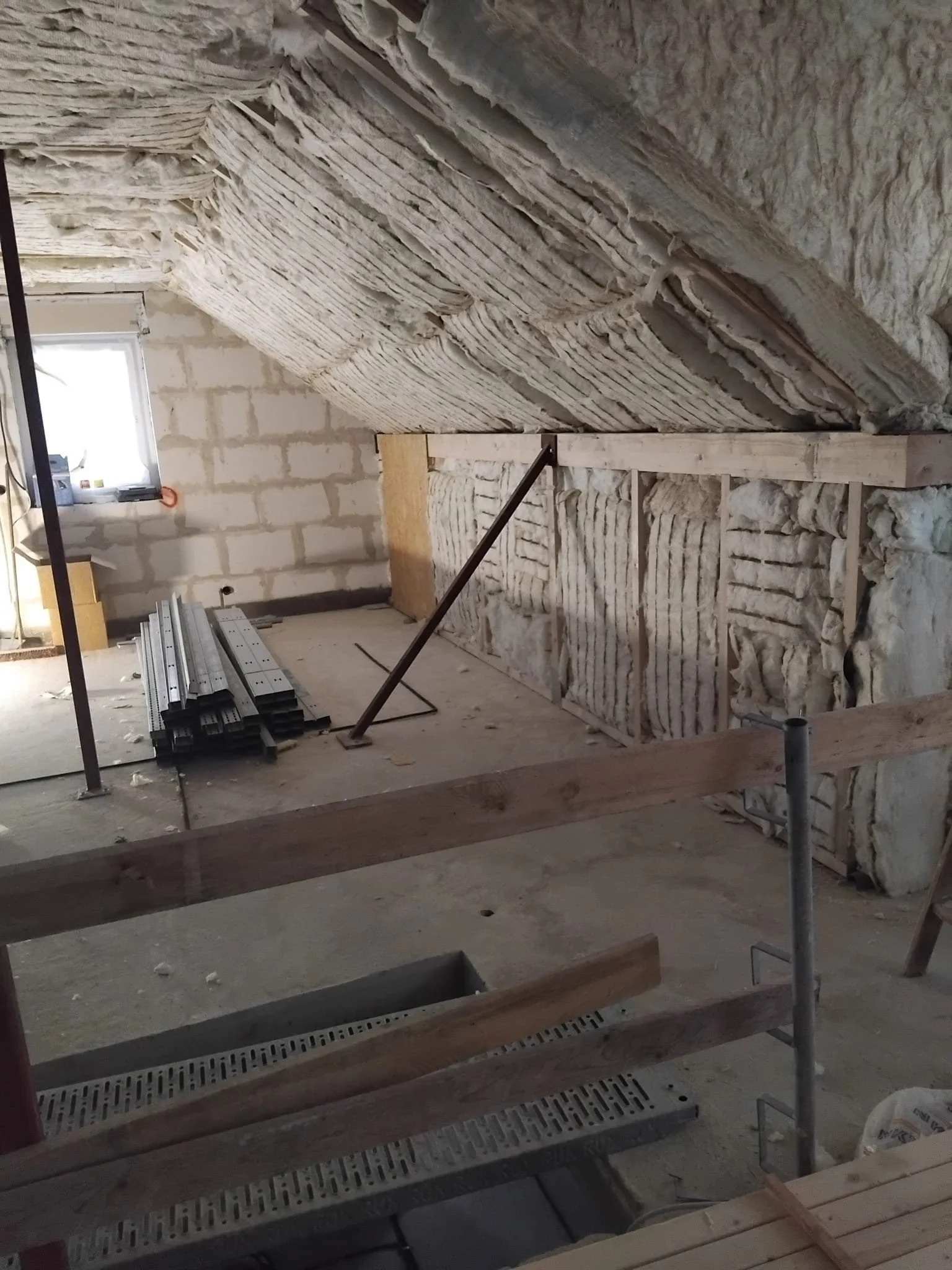 Innenansicht eines Dachbodens im Bau, mit Isolierung, Holzrahmen und Baumaterialien