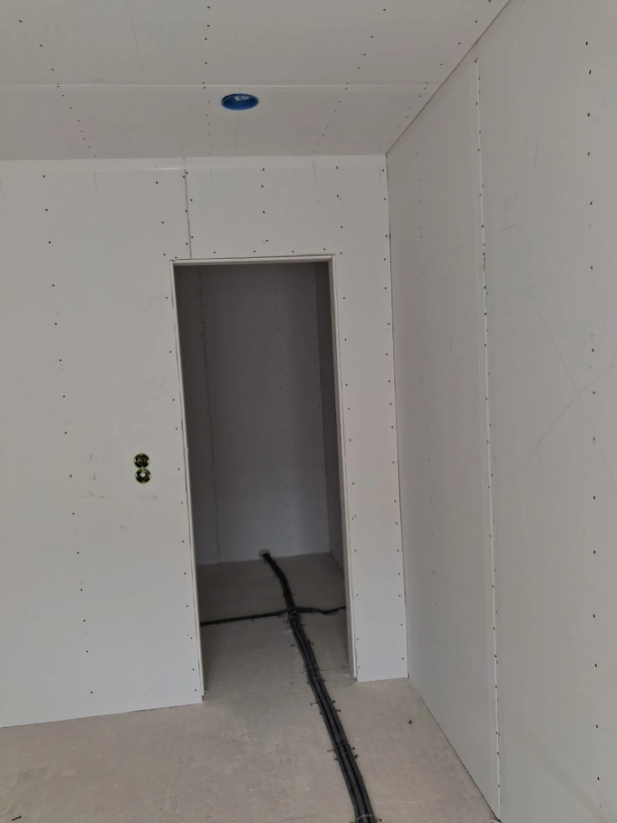 Innenraum eines Raums unter Bau- oder Renovierungsarbeiten, mit vorbereiteter Verkabelung und weißen Gipskartondecken und -wänden.