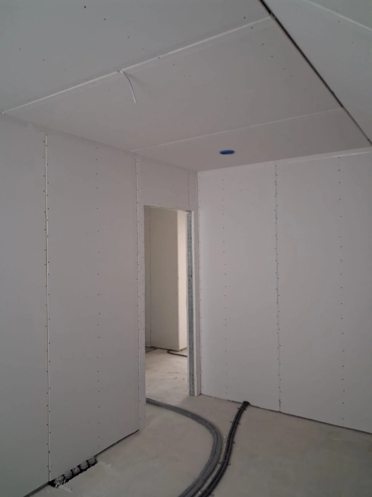 Innenraum eines im Bau befindlichen Gebäudes, Wände und Decke sind mit Gipskartonplatten verkleidet, Kabel auf Boden und durch die Wand, Türöffnung sichtbar.